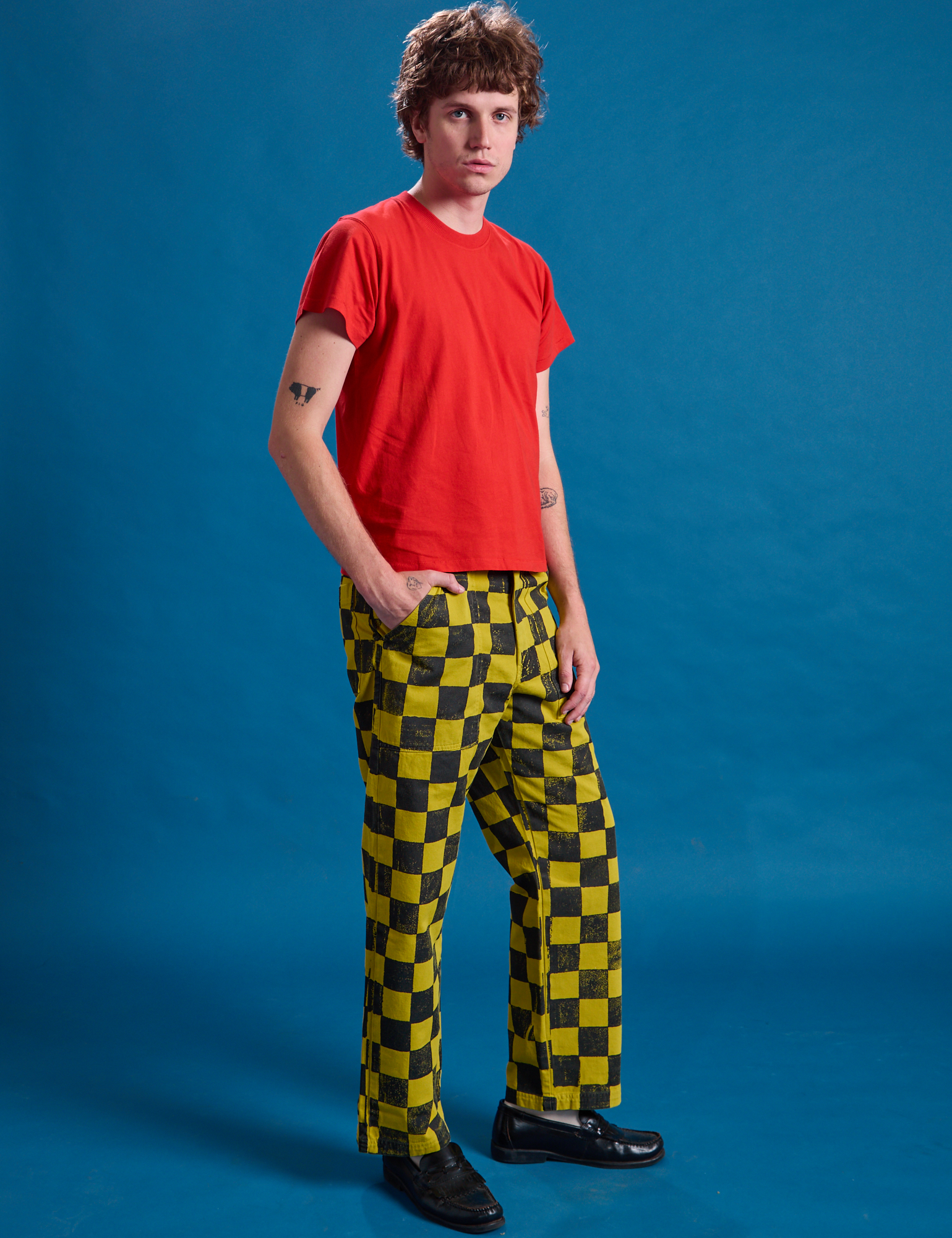Angled front view of Checkerboard Work Pants in Yellow/Black and mustang red Organic Vintage Tee on Quinn
