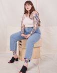 Sydney is sitting on a stack of wooden crates wearing Denim Trouser Jeans in Light Wash and Tank Top in vintage tee off-white