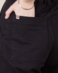 Back pocket close up of Petite Short Sleeve Jumpsuit in Basic Black. Worn by Hana with her hand in the pocket.