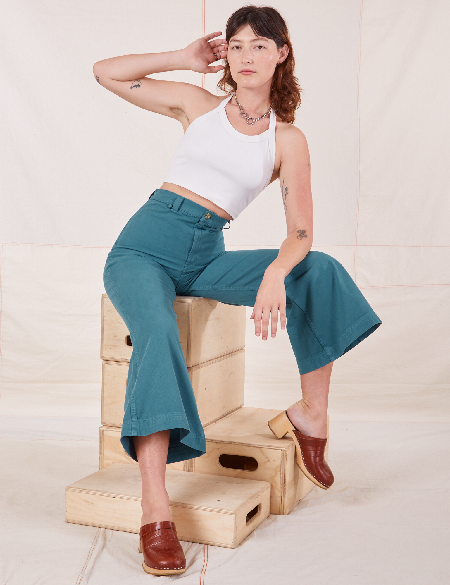 Alex is sitting on a stack of wooden crates. She is wearing Bell Bottoms in Marine Blue and Halter Top in vintage tee off-white