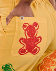 Close up of Kandia's hand in the back pocket of Gummy Bear Paintstamped Work Pants in Butter Yellow
