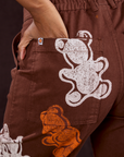 Close up of Kandia's hand in the back pocket of Gummy Bear Paintstamped Work Pants in Fudgesicle Brown
