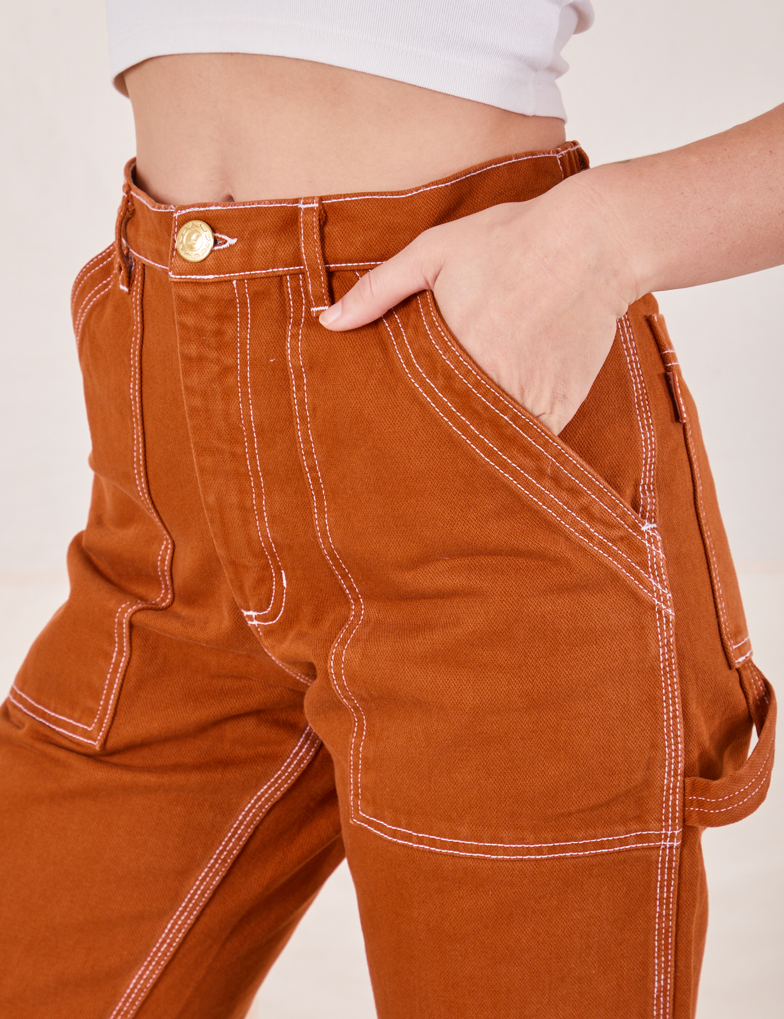 Front pocket close up of Carpenter Jeans in Burnt Terracotta. Alex has her hand in the pocket.