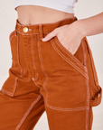 Front pocket close up of Carpenter Jeans in Burnt Terracotta. Alex has her hand in the pocket.