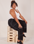 Morgan is sitting on a stack of wooden crates. She is wearing Carpenter Jeans in Black and vintage off-white Tank Top.