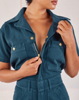 Heritage Short Sleeve Jumpsuit in Lagoon front close up. Mika is pulling down on the zipper.
