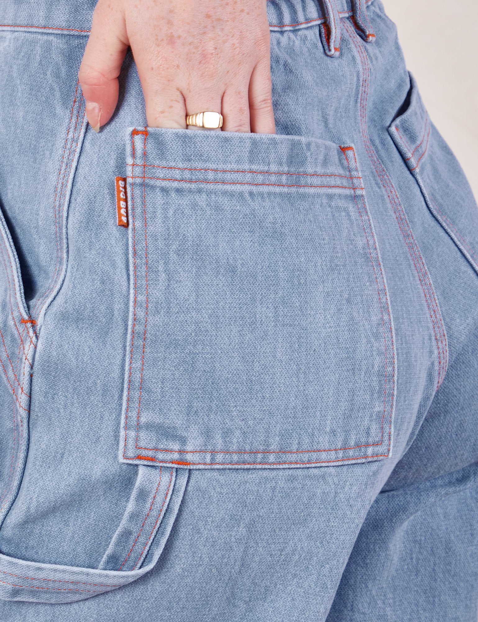 Carpenter Shorts in Light Wash back pocket close up. Margaret has her hand in the pocket.