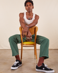 Work Pants in Dark Emerald Green on Jerrod wearing vintage off-white Tank Top. Jerrod is sitting backwards in a wooden chair with yellow cushion.