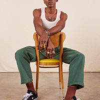 Work Pants in Dark Emerald Green on Jerrod wearing vintage off-white Tank Top. Jerrod is sitting backwards in a wooden chair with yellow cushion.