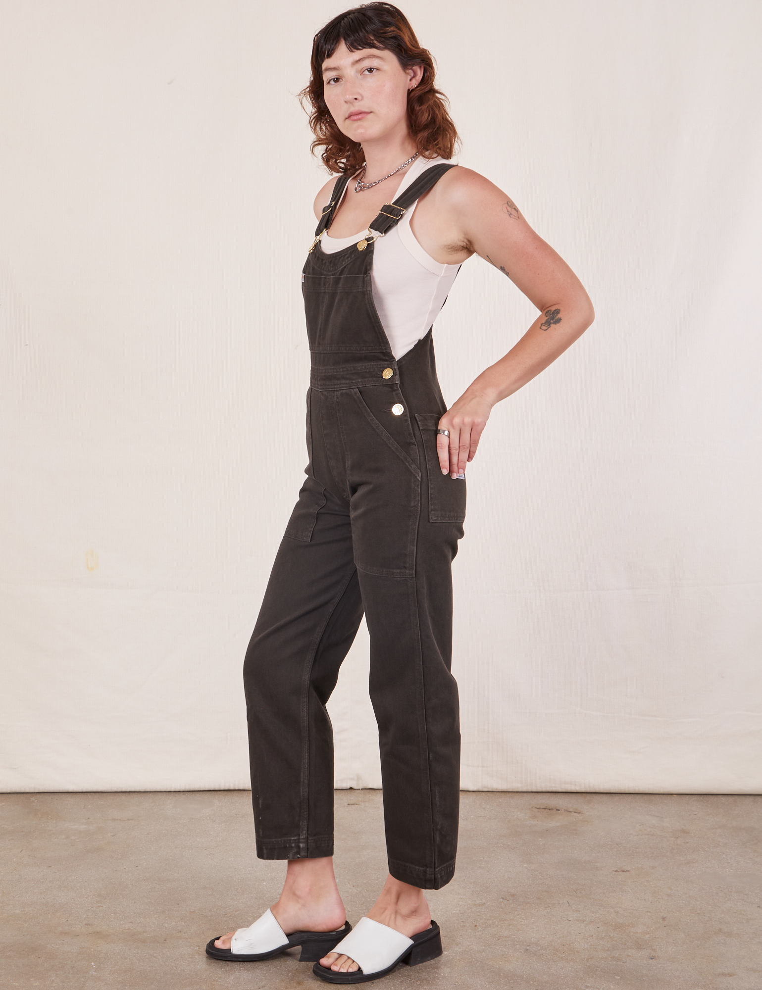 Side view of Original Overalls in Mono Espresso and Cropped Tank Top in vintage tee off-white worn by Alex.