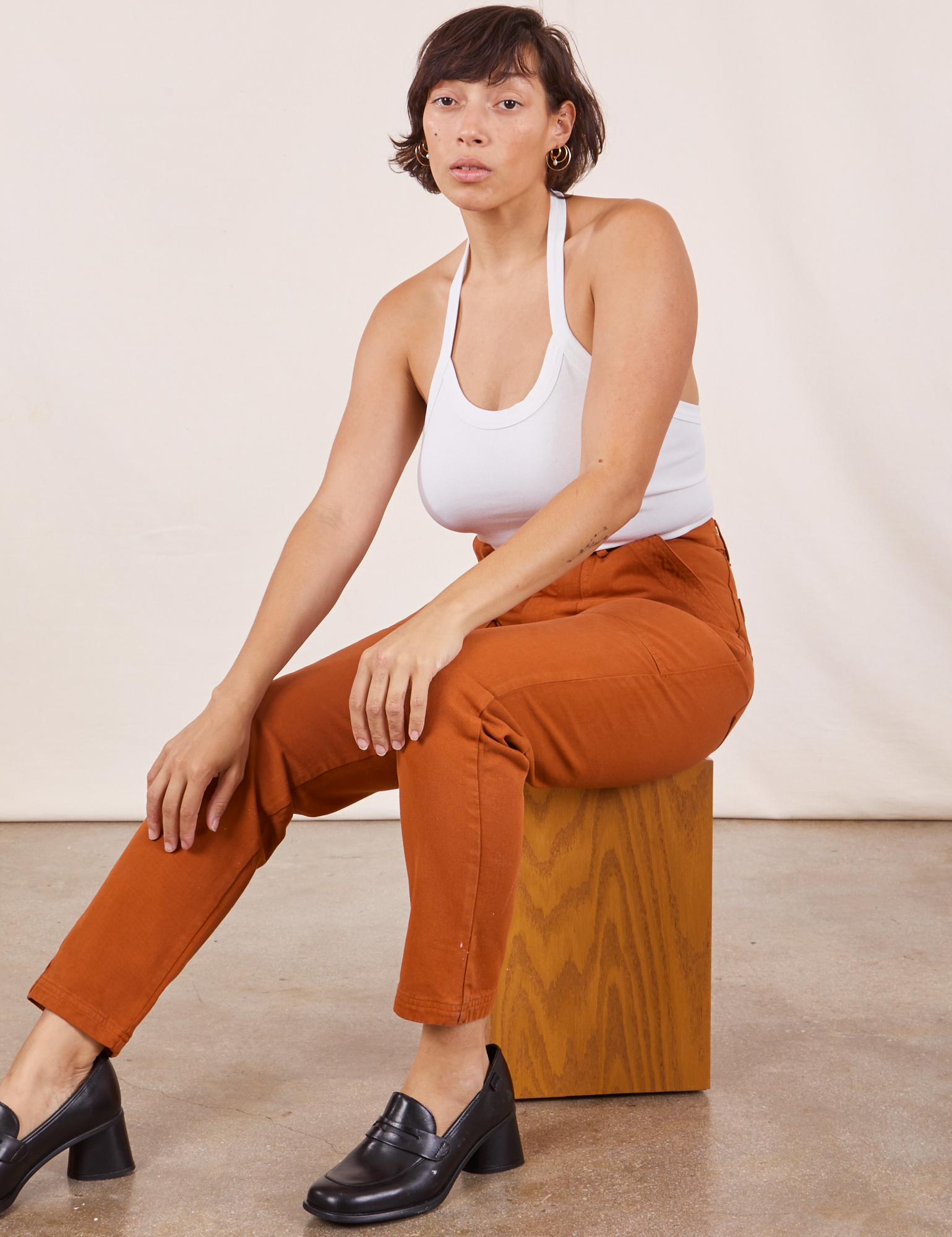 Tiara is sitting on a wooden box wearing Pencil Pants in Burnt Terracotta and Halter Top in vintage tee off-white