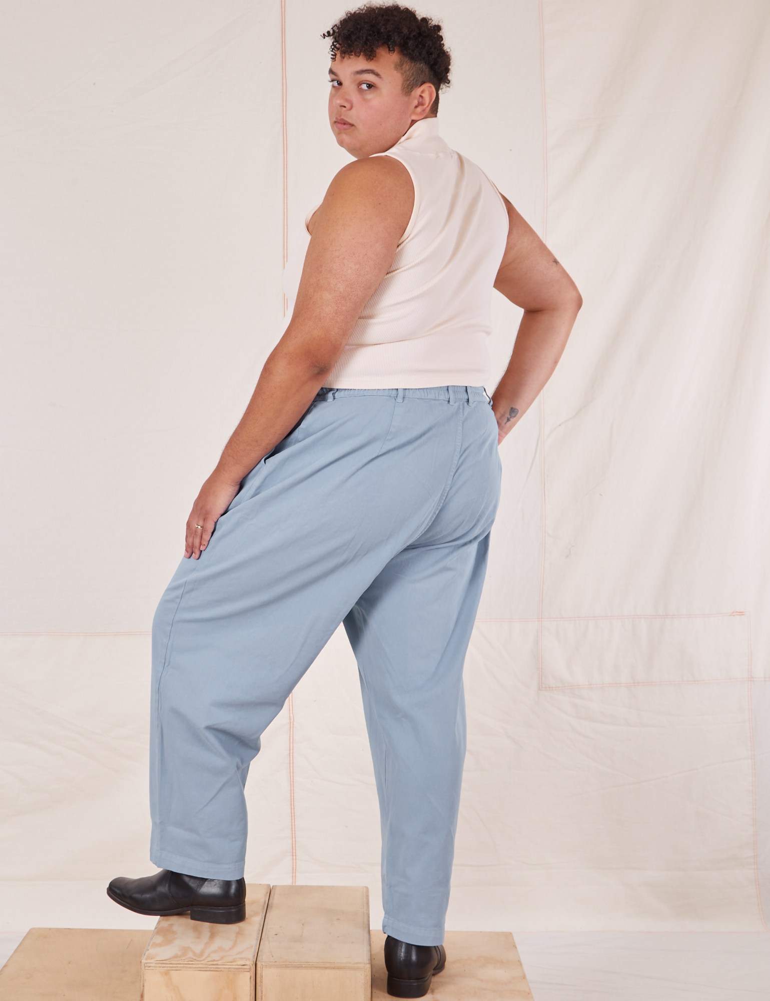 Angled back view of Heavyweight Trousers in Periwinkle and vintage off-white Sleeveless Turtleneck on Miguel