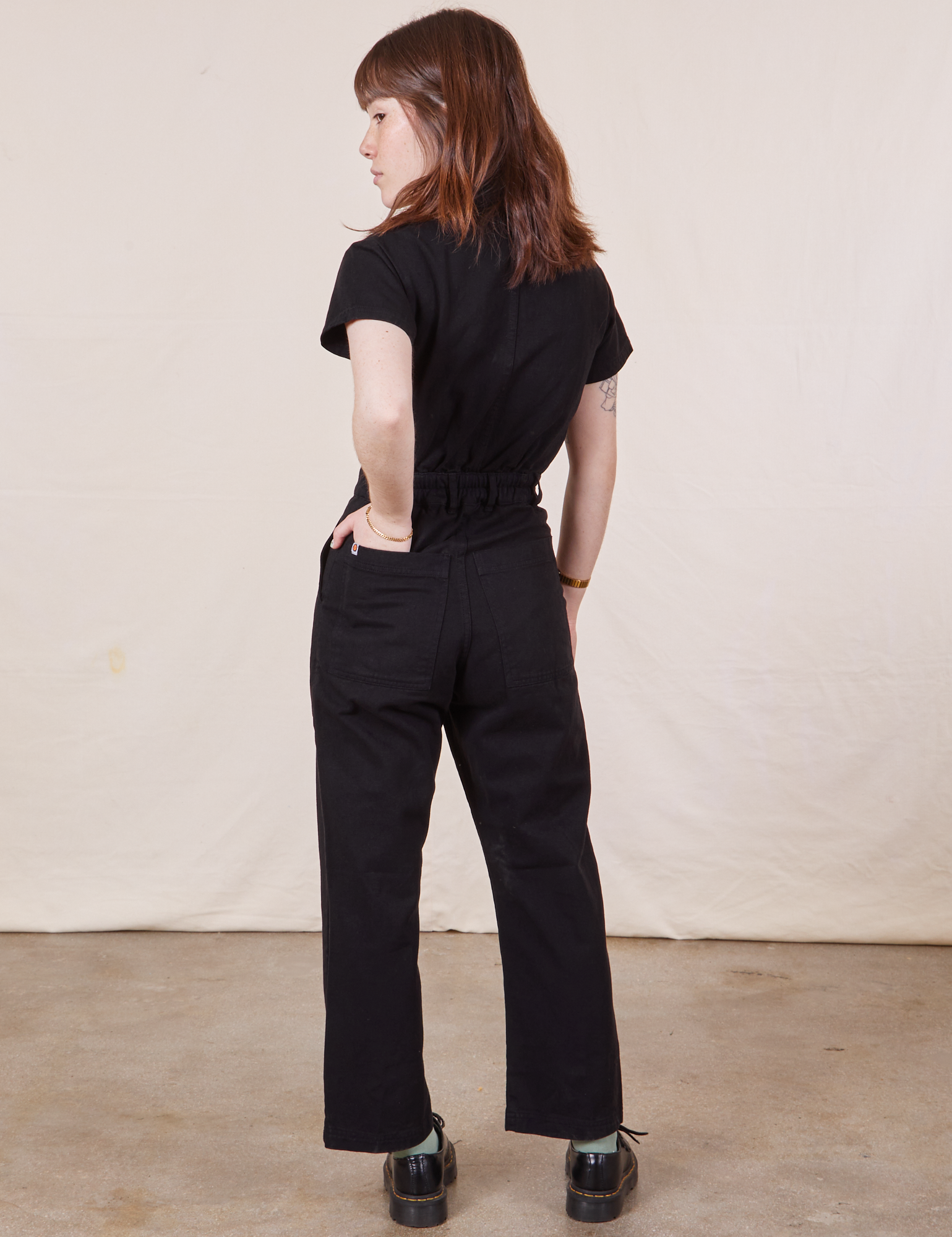 Petite Short Sleeve Jumpsuit in Basic Black back view on Hana with her hand in the back pocket.