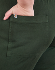 Back pocket close up of Short Sleeve Jumpsuit in Swamp Green. Marielena has her hand in the pocket.