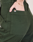 Petite Short Sleeve Jumpsuit in Swamp Green back pocket close up. Hana has her hand in the pocket.