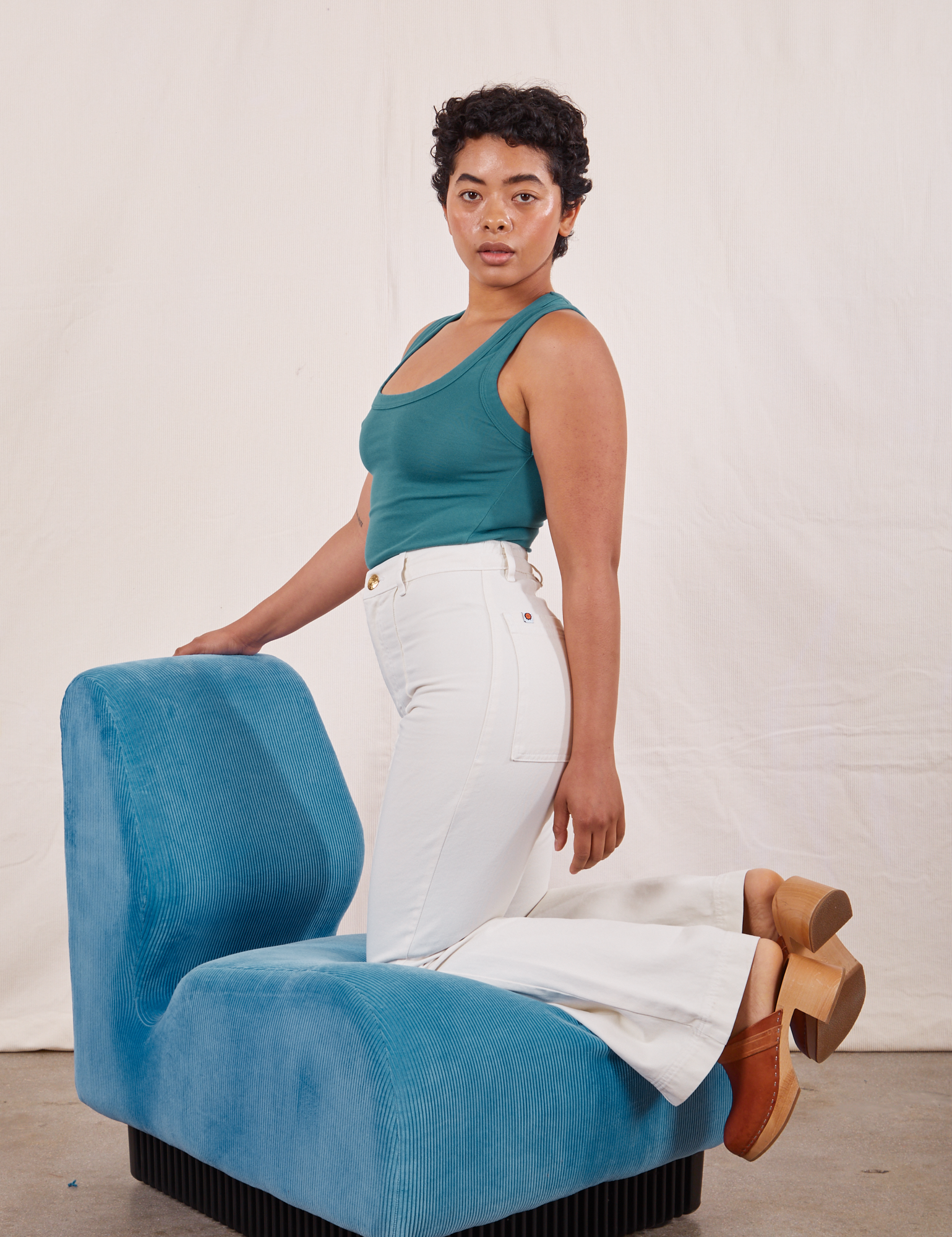 Mika is kneeling on a bright blue upholstered chair wearing Tank Top in Marine Blue and vintage tee off-white Western Pants