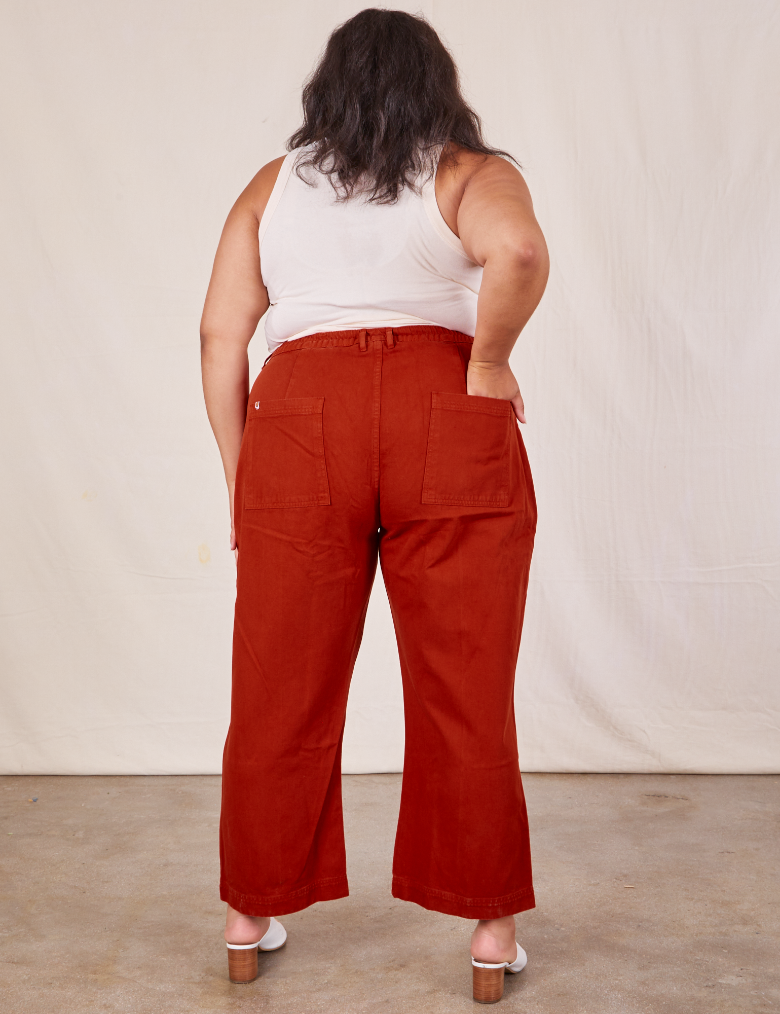 Back view of Western Pants in Paprika and Tank Top in vintage tee off-white worn by Alicia. She also has one hand in the pocket.