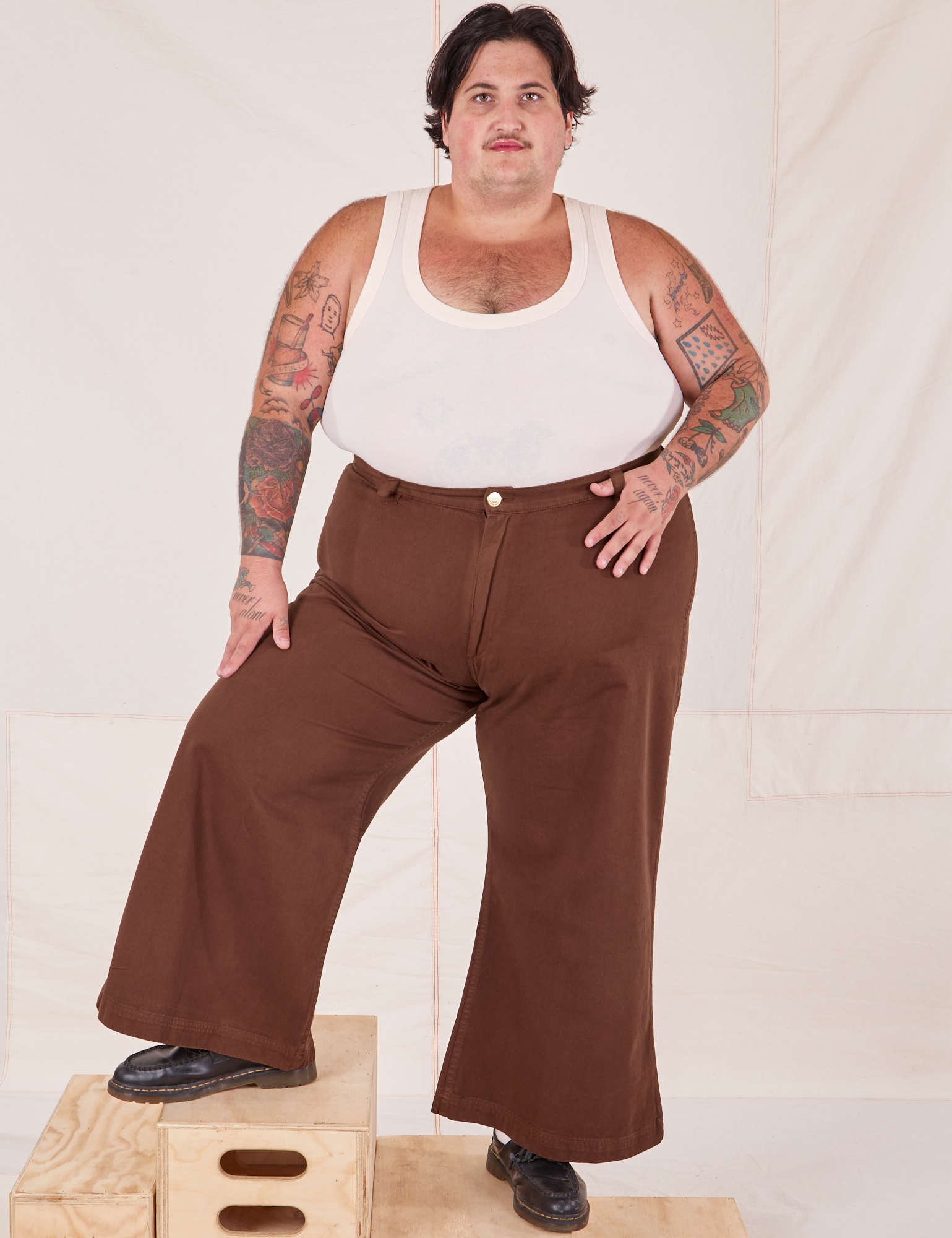 Sam is 5&#39;10&quot; and wearing 3XL Bell Bottoms in Fudgesicle Brown paired with a Tank Top in vintage tee off-white
