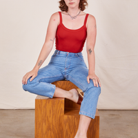 Alex is sitting on a wooden block wearing Cropped Cami in Mustang Red and light wash Frontier Jeans