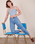 Alex is kneeling on vintage blue chairs wearing Cropped Cami in Periwinkle and light wash Frontier Jeans