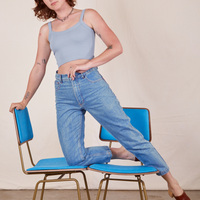 Alex is kneeling on vintage blue chairs wearing Cropped Cami in Periwinkle and light wash Frontier Jeans