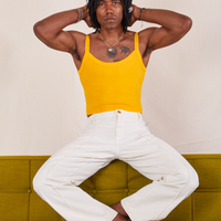 Jerrod is sitting on a olive green sofa wearing Cropped Cami in Sunshine Yellow and vintage off-white Western Pants