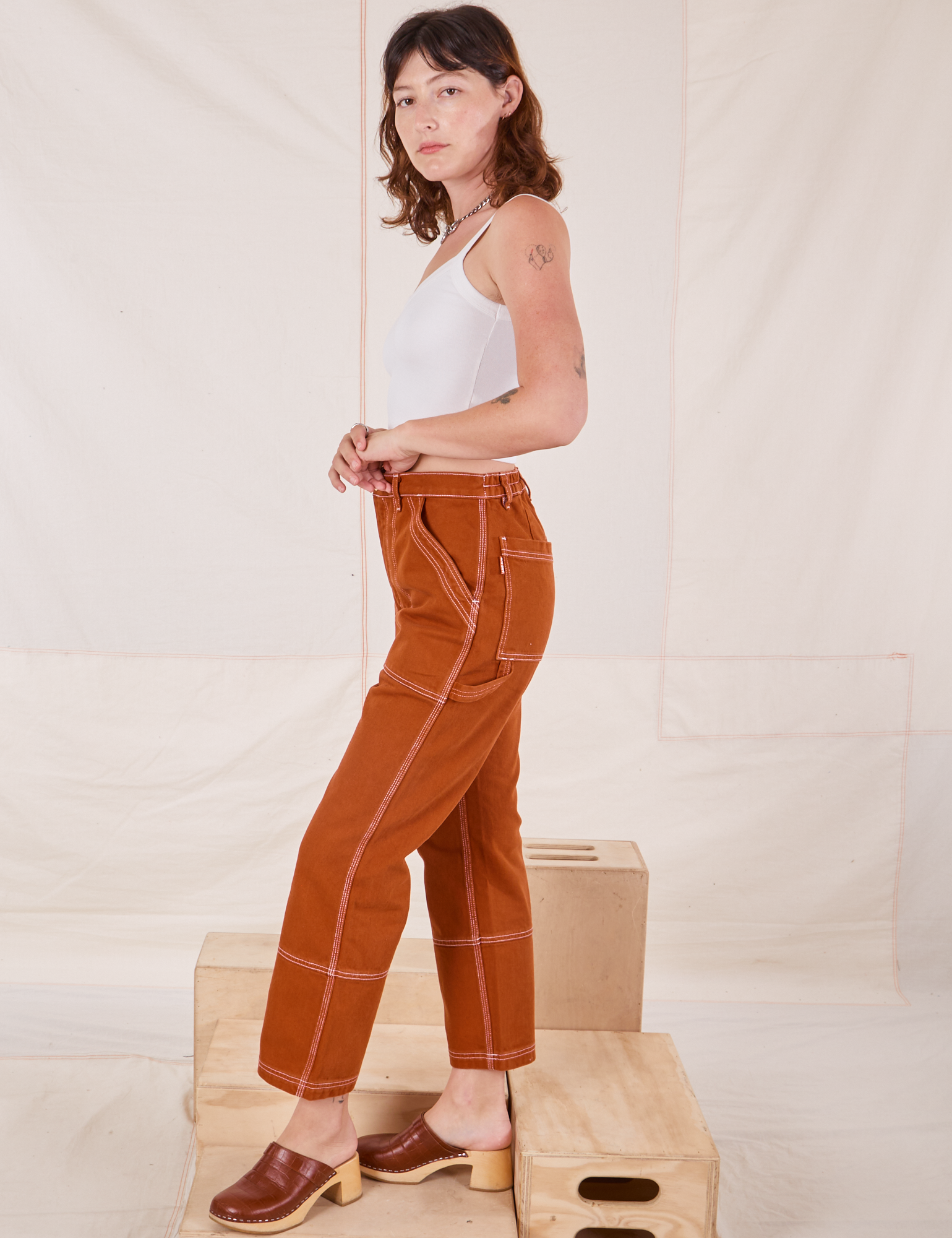 Side view of Carpenter Jeans in Burnt Terracotta and Cropped Cami in vintage tee off-white on Alex