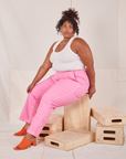 Morgan is sitting on a wooden crate wearing Carpenter Jeans in Bubblegum Pink and Tank Top in vintage tee off-white