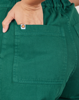 Back pocket close up of Short Sleeve Jumpsuit in Hunter Green. Tiara has her hand in the pocket.