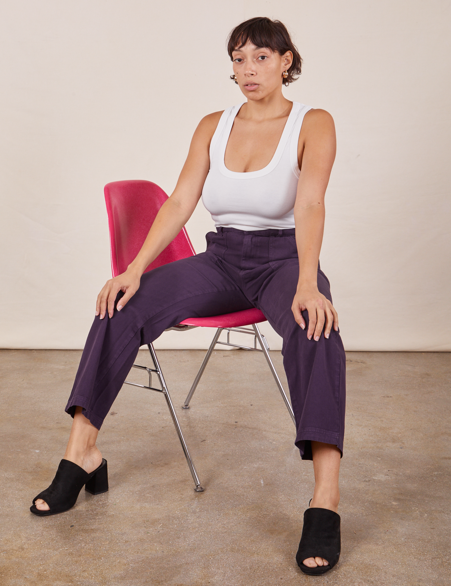 Tiara is wearing Work Pants in Nebula Purple and a Cropped Tank Top in vintage tee off-white sitting in a pink chair