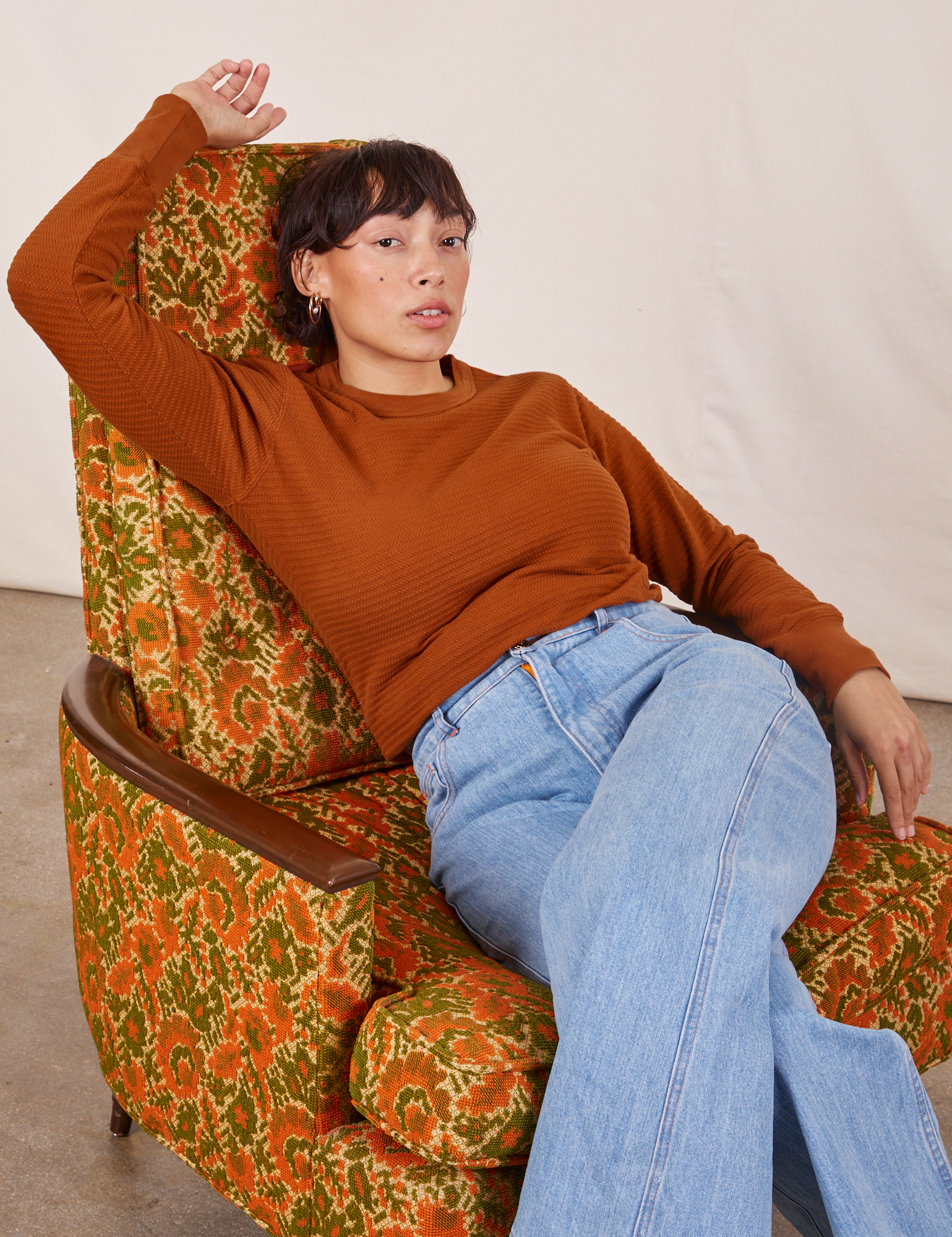 Tiara is sitting on an upholstered chair wearing Honeycomb Thermal in Burnt Terracotta