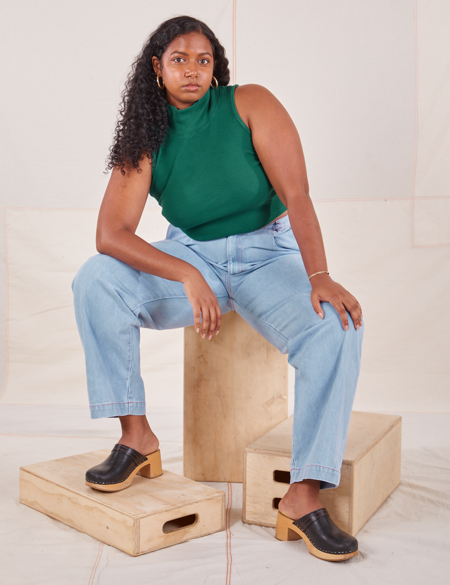 Meghna is wearing Sleeveless Essential Turtleneck in Hunter Green and light wash Denim Trousers