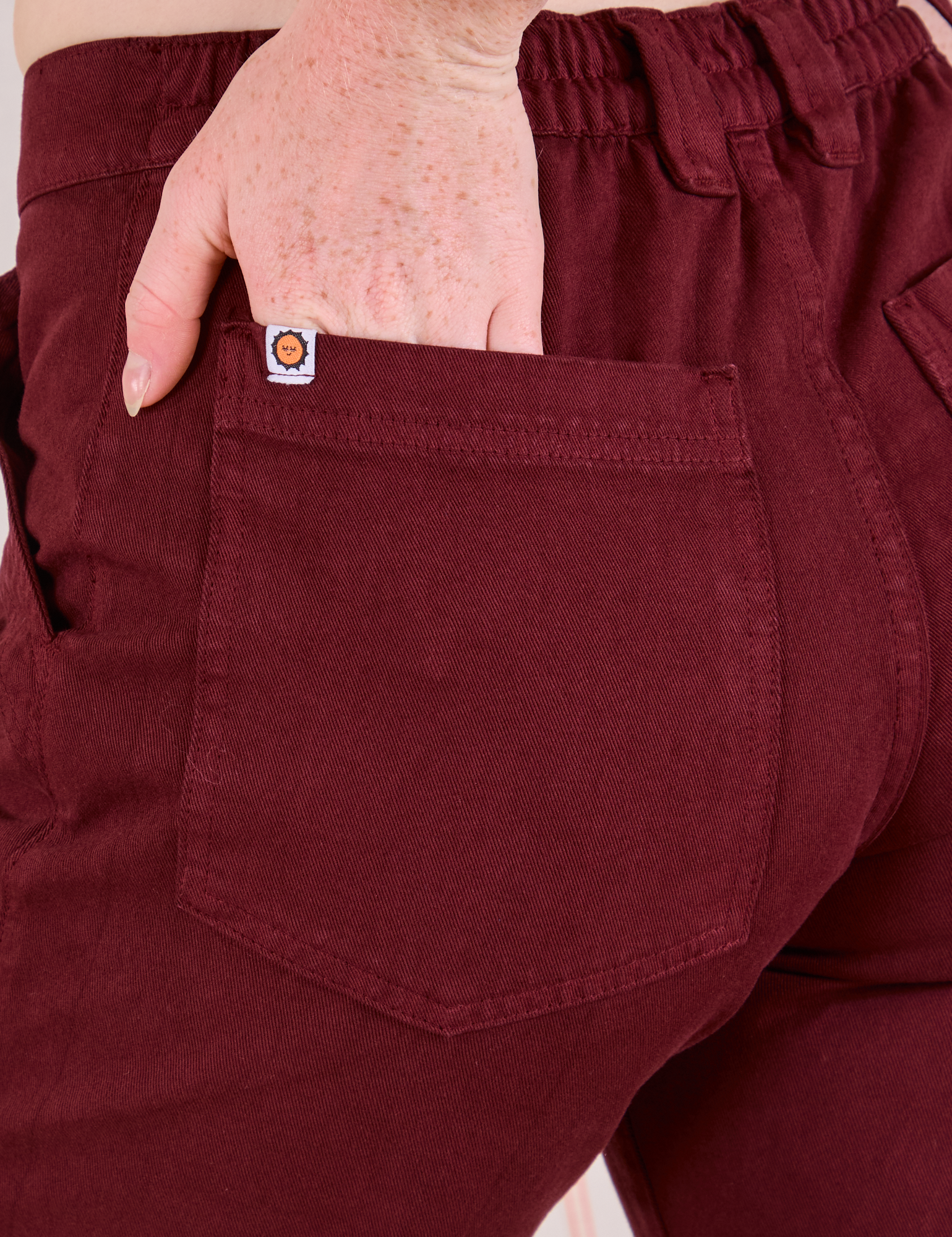 Mid-Rise Work Pants in Red Wine close up of Margaret's hand in the back pocket