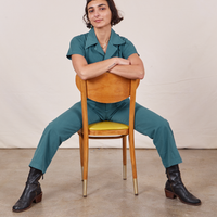 Soraya is sitting backwards on a wooden chair wearing Petite Short Sleeve Jumpsuit in Marine Blue