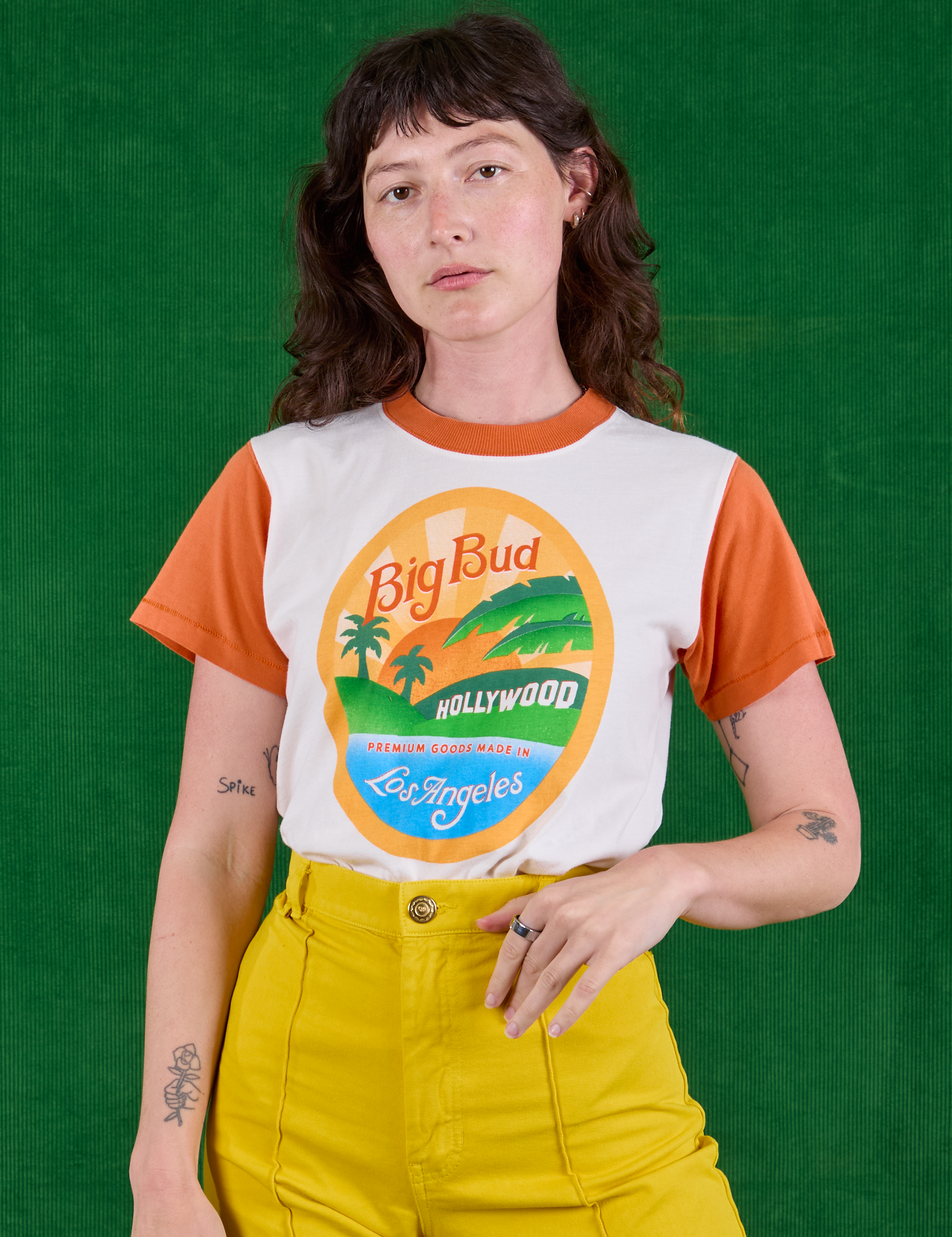 Alex is wearing Hollywood Tourist Tee tucked into golden yellow Western Pants