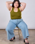 Ashley is sitting in a chair wearing Cropped Tank Top in Olive Green and light wash Indigo Wide Leg Trousers