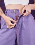 Overdyed Wide Leg Trousers in Faded Grape front close up. Alex is pulling on the zipper tab.