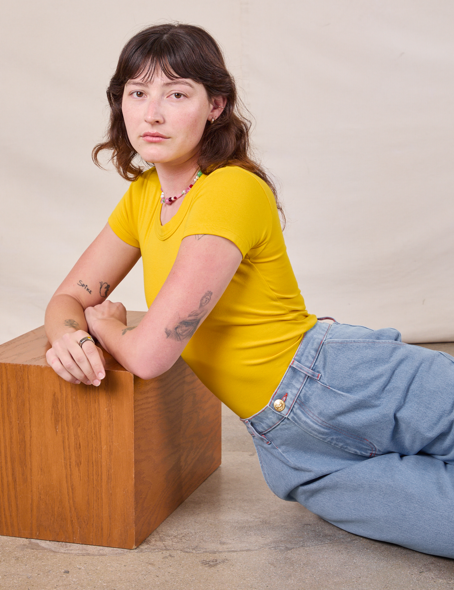 Alex is wearing Baby Tee in Golden Yellow with light wash denim Trousers