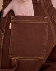 Close up of Alex's hand in the back pocket of Carpenter Jeans in Fudgesicle Brown