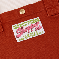 Close up of brass sun baby snap on paprika Shopper Tote Bag. Bag label with green and pink text that reads "Big Bud Press, Shopper Tote, Made in L.A. 100% Cotton Denim" on a white background
