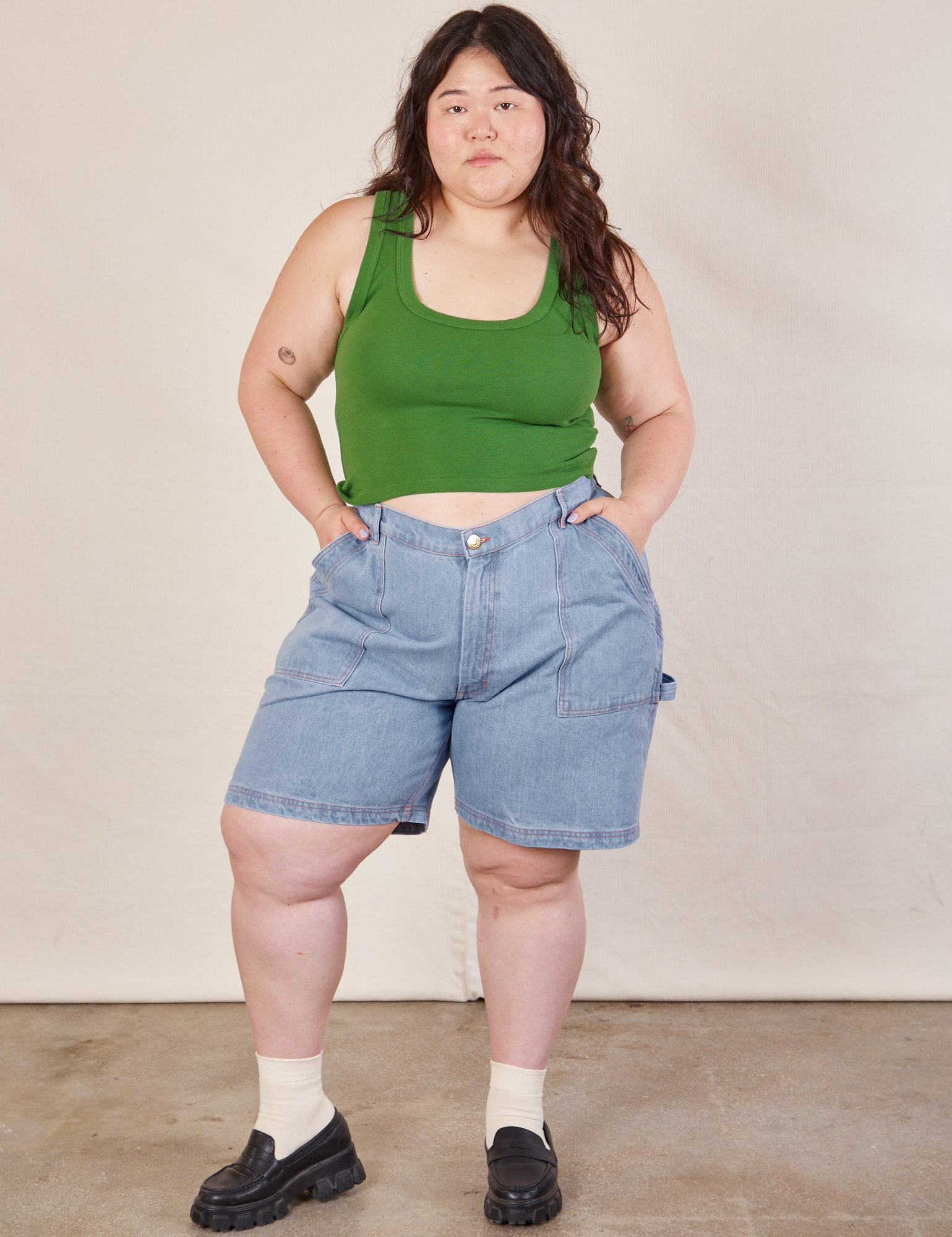 Ashley is 5'7" and wearing 1XL Carpenter Shorts in Light Wash paired with lawn green Cropped Tank