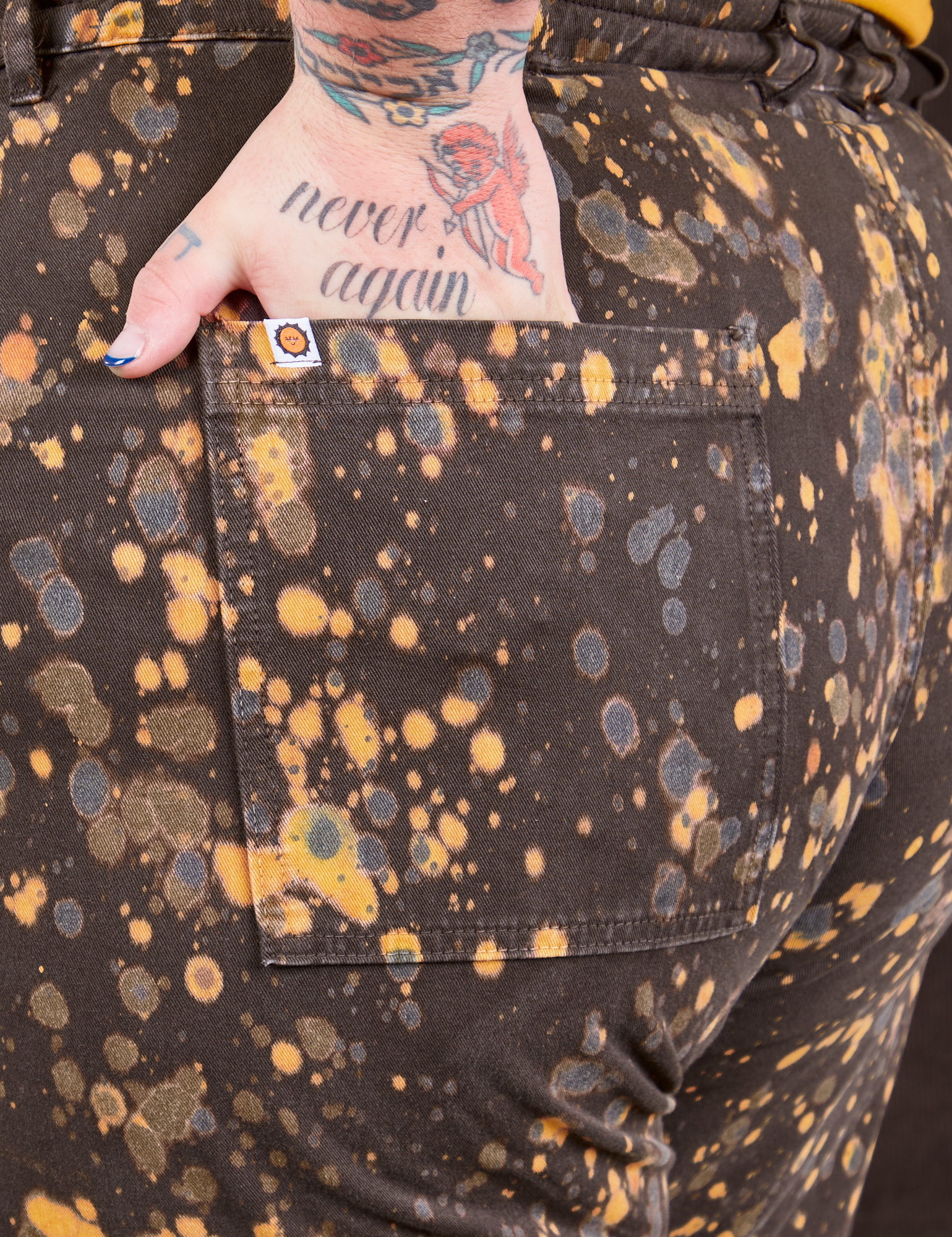 Marble Splatter Work Pants in Espresso Brown back pocket close up. Sam has their hand in the pocket.