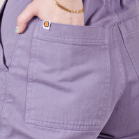 Back pocket close up of Petite Short Sleeve Jumpsuit in Faded Grape. Hana has their hand in the pocket.