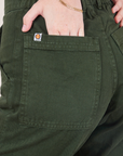 Petite Work Pants in Swamp Green back pocket close up. Hana has her hand in the pocket.