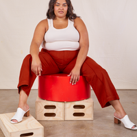 Alicia is sitting on a circular platform wearing Western Pants in Paprika and a vintage off-white Tank Top