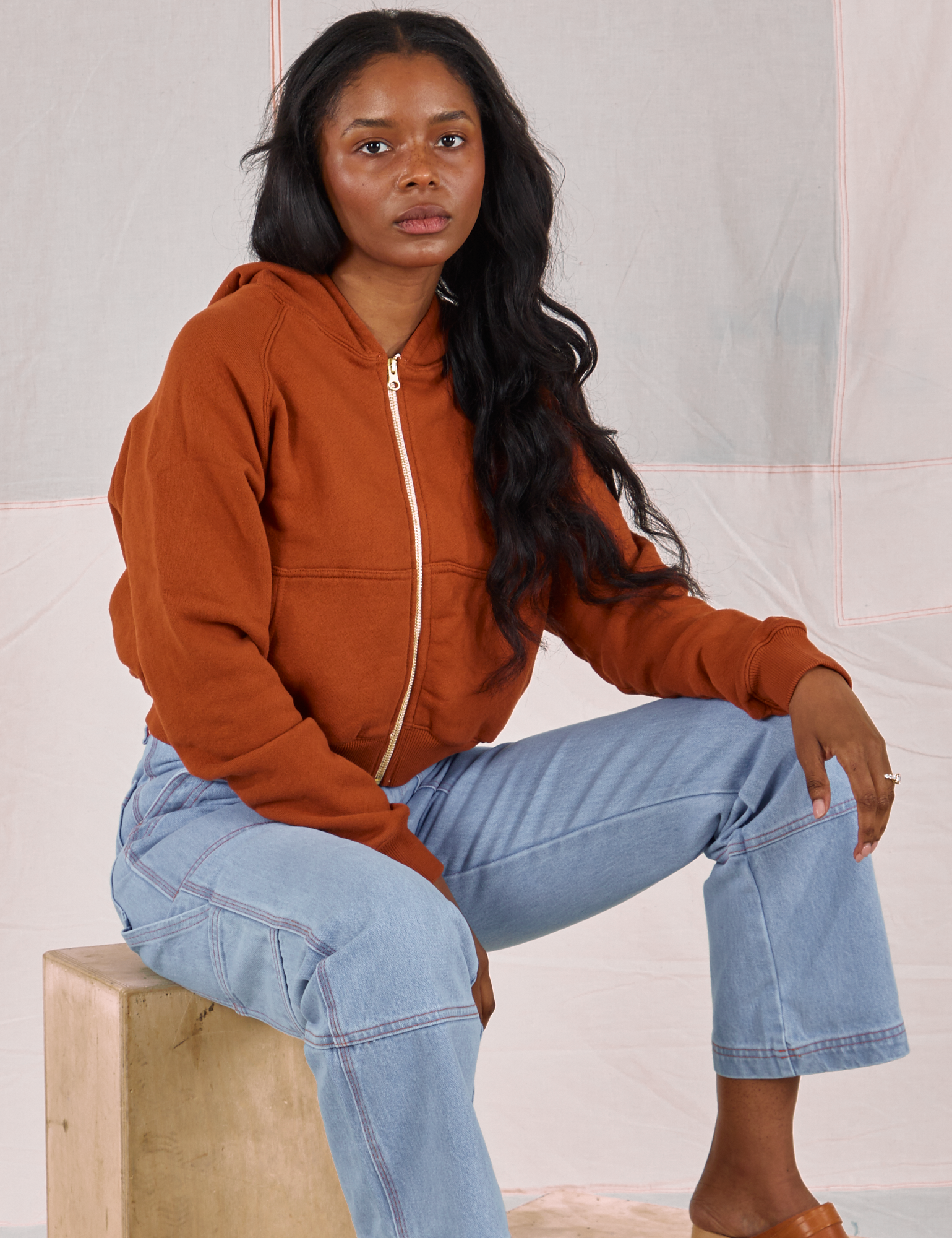 Kandia is wearing Cropped Zip Hoodie in Burnt Terracotta and light wash Carpenter Jeans