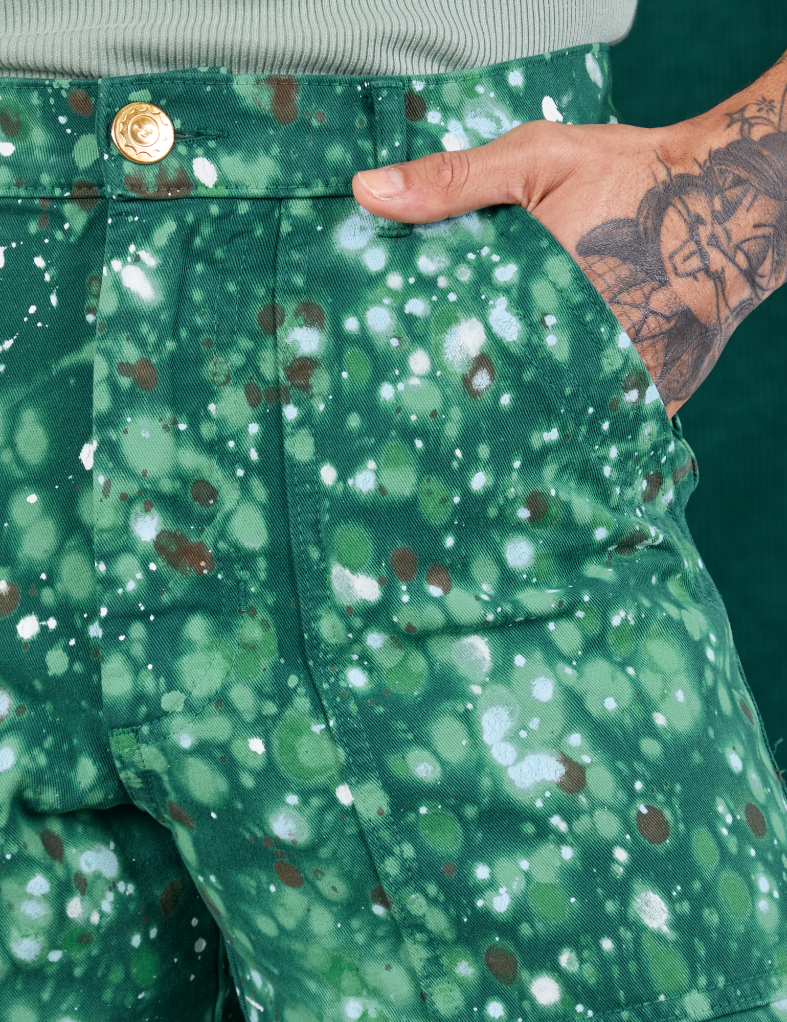 Front pocket close up of Marble Splatter Work Pants in Hunter Green. Jesse has their hand in the pocket.