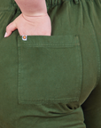 Back pocket close up of Petite Short Sleeve Jumpsuit in Dark Emerald Green. Ashley has her hand in the pocket