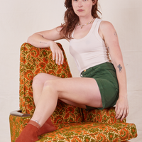 Alex is sitting in the arm chair of a vintage floral upholstered chair. Alex is wearing Classic Work Shorts in Dark Emerald Green and a vintage off-white Tank Top