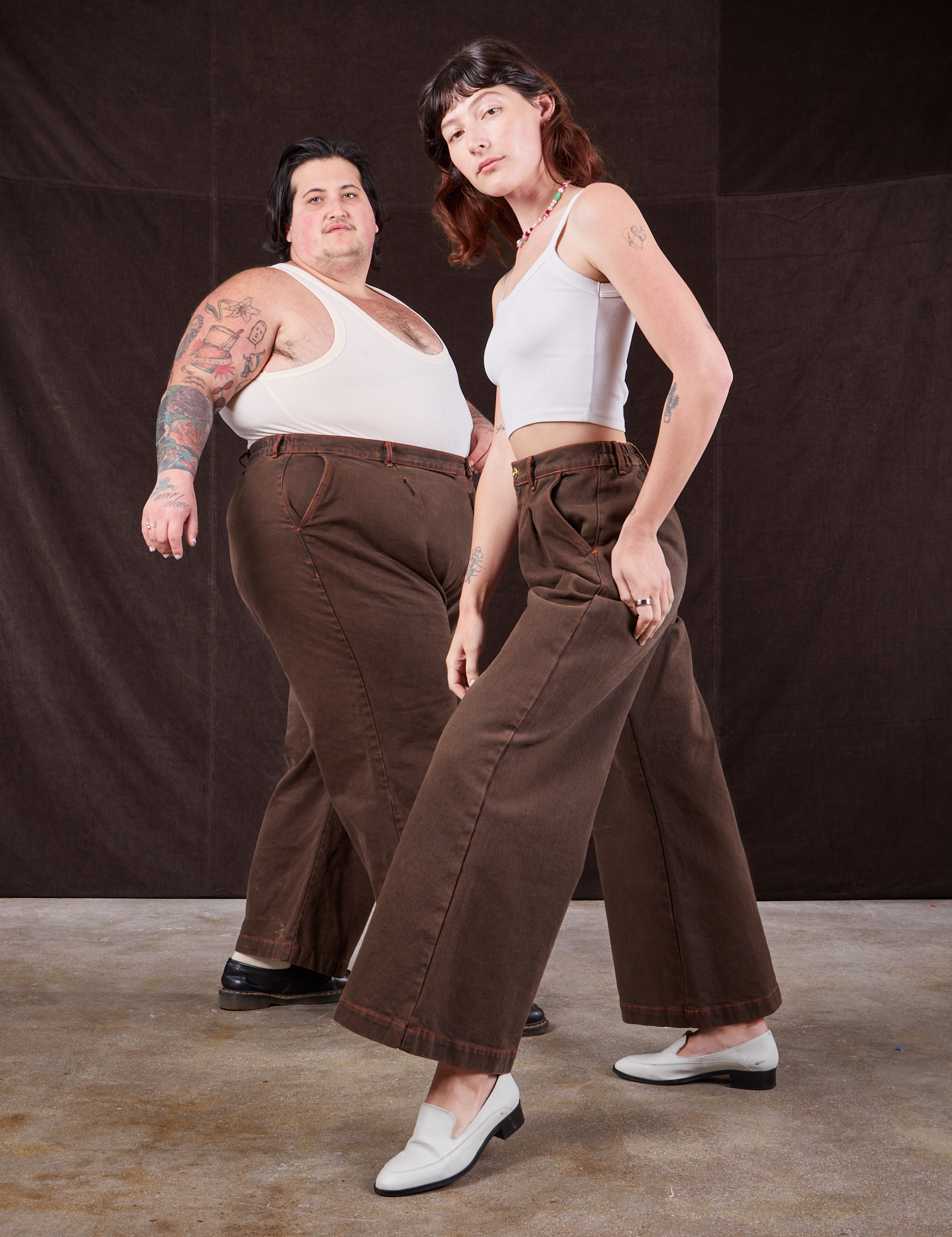Alex is wearing Overdyed Wide Leg Trousers in Brown and Cropped Cami in vintage tee off-white. Sam is behind her wearing the same pants with a Tank Top in vintage tee off-white